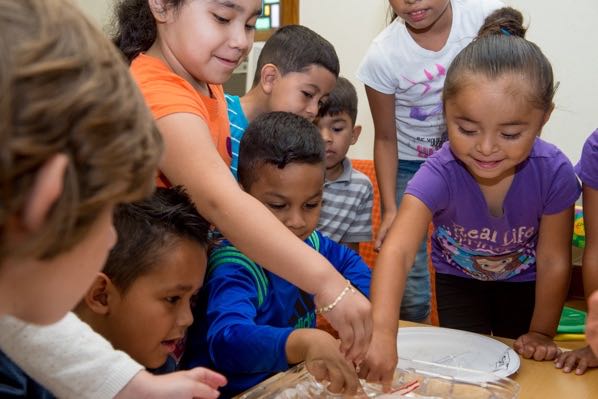Children gather around a tray of water during a lesson at Brilliant Detroit