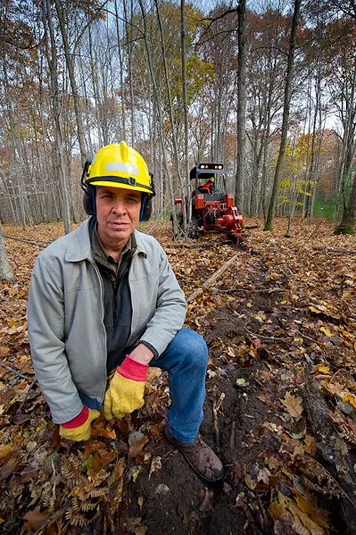 Michigan DNR forest health specialist Roger Mech, with vibratory plow in the background used to separate oak-wilt-infected tree roots from the roots of healthy oak.