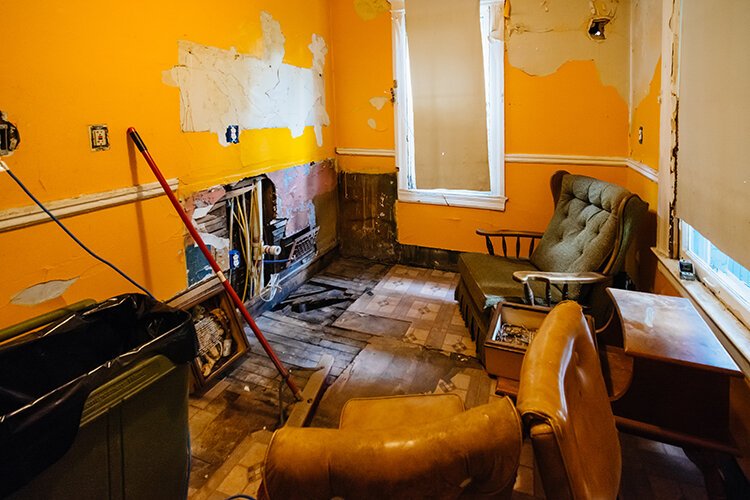 Paint peels from the walls while the house's bones show through a portion of disintegrated drywall.