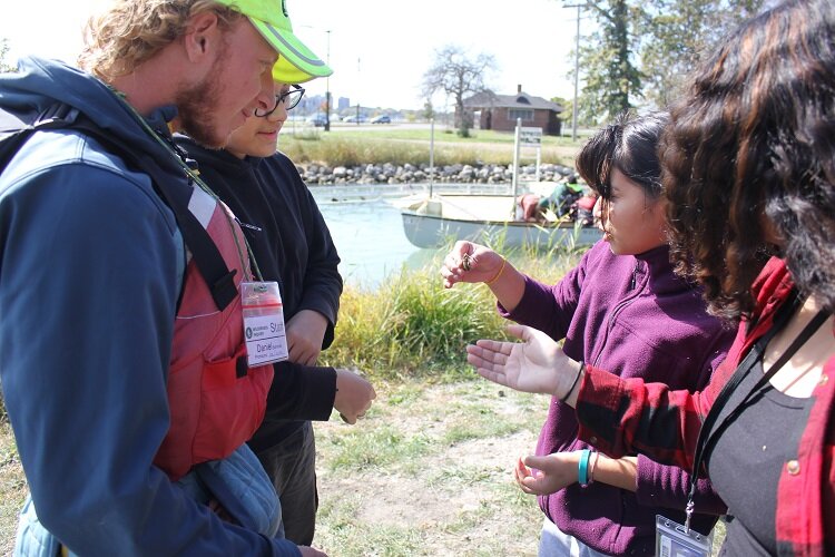 An Academy of the Americas student holds a crayfish that one of them found in the rocks along the shoreline after canoeing.