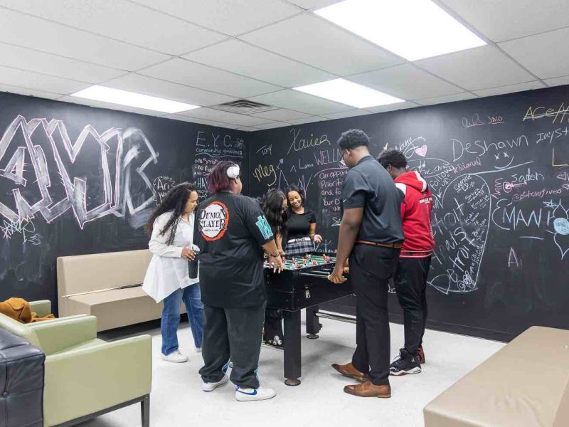 Caitlin Crutcher (white shirt) plays foosball with youth before programming at Eastside Community Network