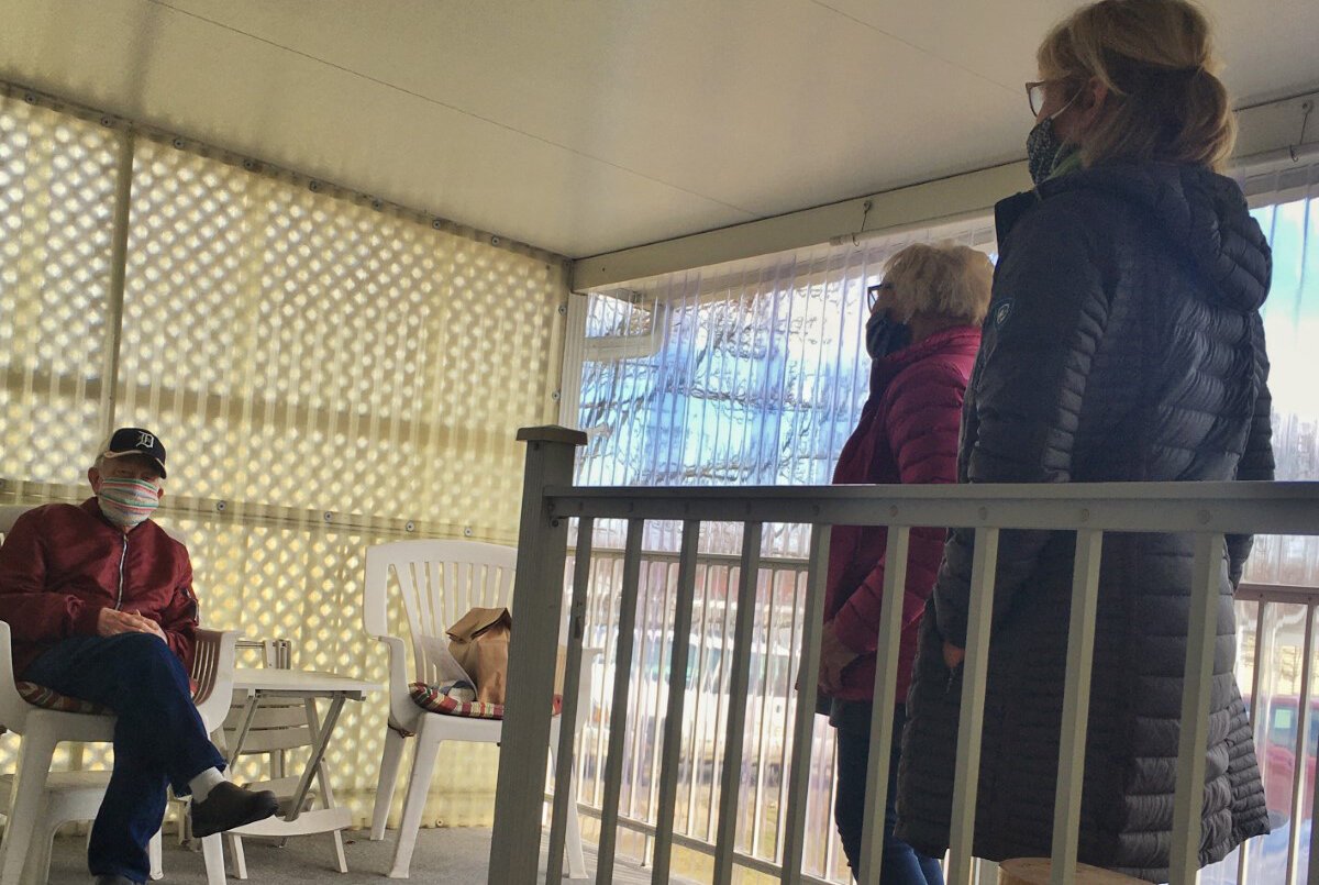 Meals on Wheels volunteers Annie and Linda chat with client Quint at a safe distance.